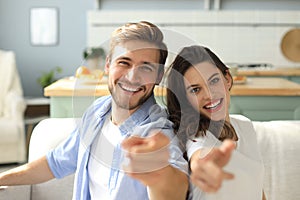 Portrait of cute young couple pointing and laughing, sitting in sofa