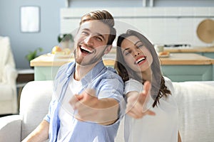 Portrait of cute young couple pointing and laughing, sitting in sofa