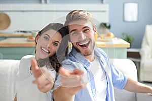 Portrait of cute young couple pointing and laughing, sitting in sofa