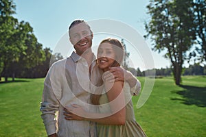 Portrait of cute young couple smiling at camera, posing together outdoors while standing in the park