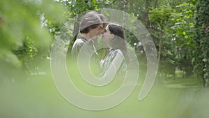 Portrait cute young couple tenderly hugging and kissing in the background, blurred leaves in the foreground. Happy girl