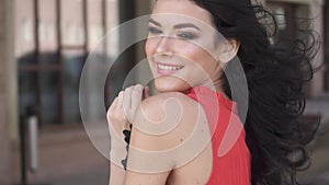 Portrait of a cute young girl with beautiful make-up. Brunette in red dress on the street. slow motion