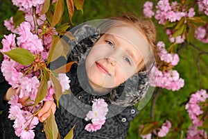 Portrait of a cute young girl that resting in the shade of blooming Japanese cherry sakura