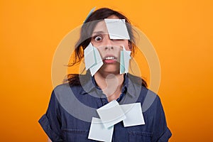 Portrait of cute young woman overwhelmed of work with sticky notes on her over yellow background in studio