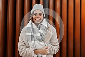 Portrait of a cute young woman with a positive smile in a fashionable knitted hat in an elegant faux fur coat with a vintage