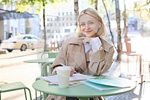 Portrait of cute young woman, student revising for exam in cafe, drinking coffee and studying, doing homework