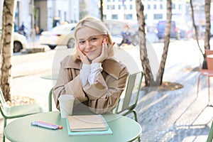 Portrait of cute young woman, student revising for exam in cafe, drinking coffee and studying, doing homework