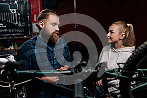 Portrait of cycling repairman having conversation with blonde female client, talking about problem of bicycle detected