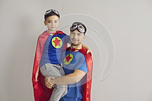 Portrait of dad and son dressed as superheroes standing in studio with gray background