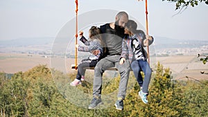 Portrait of dad swinging with daughters on a swing under a tree.