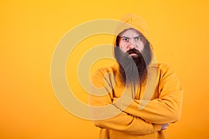 Portrait of dangerous man with long beard wearing a hoodie over yellow background