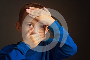 Portrait of dark-haired boy covering his face with his hands on a dark background photo