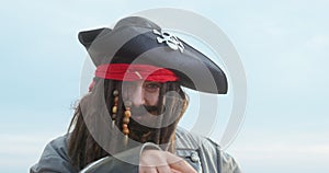 Portrait of dashing drunken pirate in wig with dreadlocks and cocked hat, who points at something with index finger and