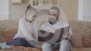 Portrait of daughter and her father sitting in living room and looking photo album with good memories and funny stories