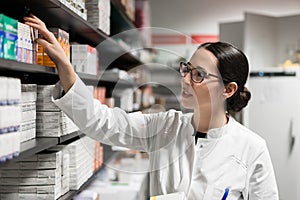 Dedicated pharmacist taking a medicine from the shelf during work photo