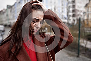 Portrait of deeply upset young woman on the street in a warm coat touching her head in mental paint. depression concept