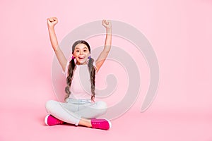 Portrait of delighted child raise fists scream shout yeah sitting dressed white pants trousers  over pink