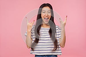 Portrait of delighted crazy girl with long hair in striped t-shirt showing rock and roll punk gesture