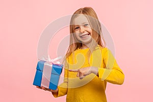 Portrait of delighted happy cute little girl pointing at gift box, boasting birthday present and smiling joyfully photo