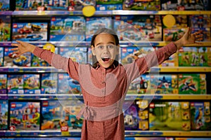 Portrait of delighted little girl child standing with toys showcases behind back