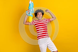 Portrait of delighted positive person hold water gun raise fist isolated on yellow color background