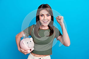 Portrait of delighted successful person hold money bank pig raise fist isolated on blue color background