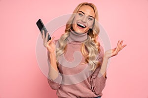 Portrait of a delighted young woman using mobile phone, isolated over pink background