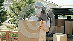 Portrait of delivery girl wearing face mask holding parcel near van outdoors during pandemic