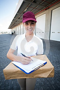 Portrait of delivery woman is holding a cardboard box and smiling to the camera