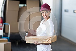Portrait of delivery woman is holding cardboard box and smiling to the camera