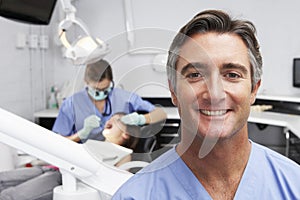 Portrait Of Dental Nurse With Dentist Examining Patient In Background