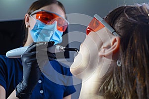 Portrait of a dentist doctor performing the procedure of professional teeth whitening using ultraviolet radiation. Patient and