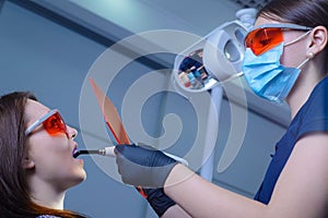 Portrait of a dentist doctor performing the procedure of professional teeth whitening using ultraviolet radiation. Patient and