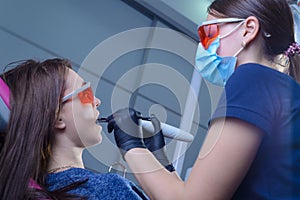 Portrait of a dentist doctor performing the procedure of professional teeth whitening using ultraviolet radiation. Patient and
