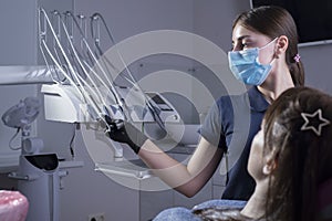 Portrait of a dentist, in a medical mask, holds a dental tool in his hand, the patient sits in a chair. Prevention and treatment