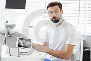 Portrait of dentist showing x-ray on tablet screen in modern dental clinic