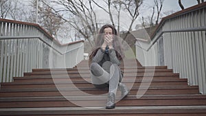Portrait of depressed Caucasian girl sitting on stairs in city park and crying. Beautiful brunette woman having problems