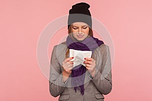 Portrait of depressed flu-sick woman in warm hat and scarf holding tissue, suffering runny nose, sneeze