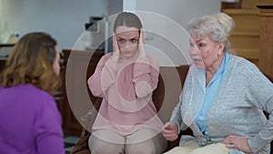 Portrait of depressed frustrated Caucasian young woman closing ears with hands as mother and grandmother quarrelling