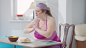 Portrait of depressed obese woman with hands wrapped with measuring tape crying eating unhealthy chips with mouth