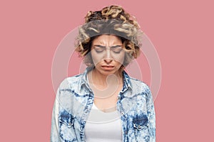 Portrait of depressed sad alone young woman with curly hairstyle in casual blue shirt standing, closed eyes and holding head down