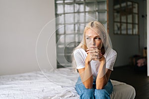 Portrait of depressed woman sitting alone at home and looking away with sad expression holding hands on chin, deep