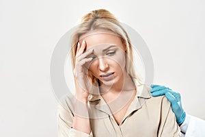 Portrait of depressed young woman visiting doctor. Doctor in blue sterile gloves supporting and comforting upset female
