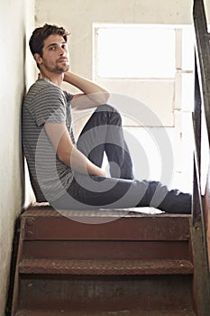 Portrait, depression and lonely with a man on a staircase in his home, sitting on the landing by a window. Alone, mental