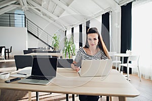 Portrait of a designer working home on new ideas. A dark hair braided woman is sitting at a white table in casual