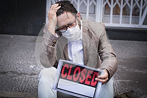Portrait of desperate man wear medical mask for coronavirus economy crisis with closed business and for sale panel - concept of