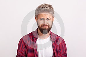 Portrait of desperate young man with beard sadly looking at camera and frowning, pursing lips