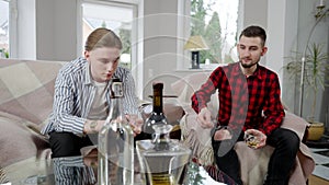 Portrait of desperate young man complaining problems to friend. Two handsome Caucasian friends drinking alcohol and