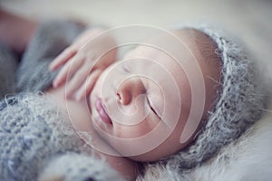 Portrait detail newborn sleeping baby on gray furry rabbit blanket with knitted woolen cap and with knitted wooll toy.