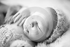 Portrait detail newborn sleeping baby on gray furry rabbit blanket with knitted woolen cap and with knitted wooll toy. Black and w